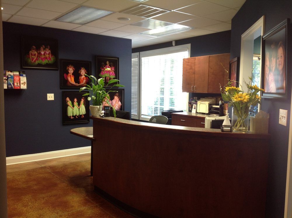 Reception area with dark blue walls, wooden front desk, framed artwork, and potted plant.