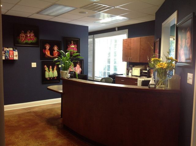 Reception area with dark blue walls, wooden front desk, framed artwork, and potted plant.